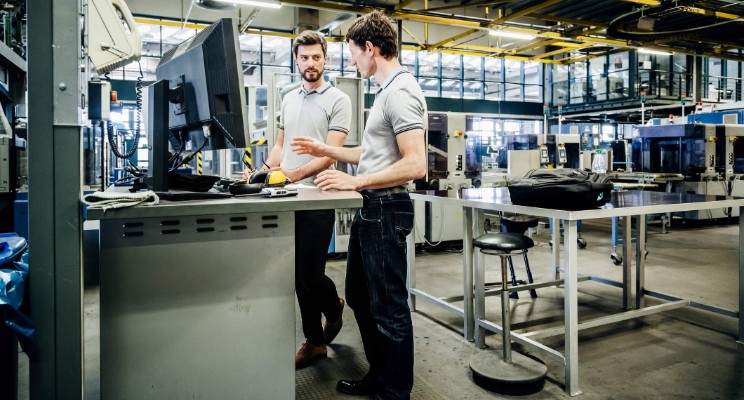 dos hombres con perfil de ingeniero industrial laborando en una fábrica